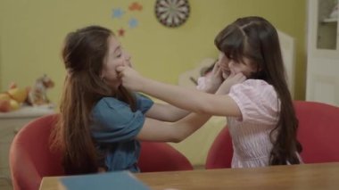 2 little girlfriends who love each other very much pinch each other's nose and cheeks in the nursery. Portrait of friends who love each other very much and have fun together.