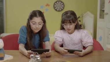 Two little girl friends playing online games with smartphones at home daycare. Children internet addiction. Portrait of girls playing games with smartphones.