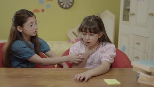 かわいい女の子たちが部屋のテーブルに座っている 少女は激しく咳をし 攻撃中に手で口を覆っていた 小児の季節性ウイルス性および感染症 — ストック動画