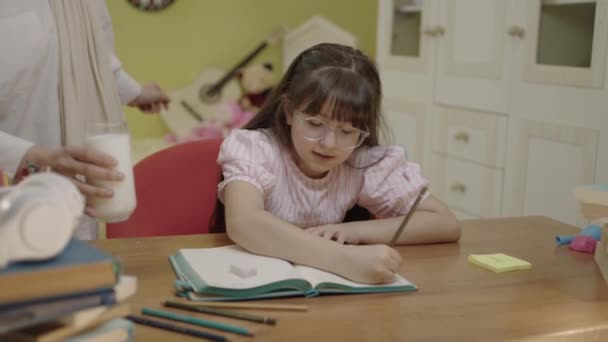 スマート小学生の女の子を書くことを学ぶ 数学の宿題をやって 自宅の机に座っている 愛しの頭皮の母親もたらすミルクのために彼女の女の子へ飲みながら彼女の学校の仕事 — ストック動画