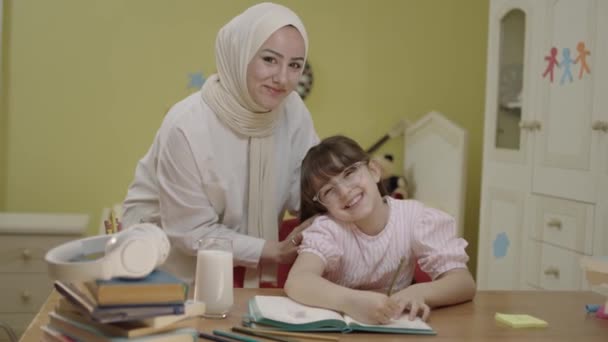 スマート小学生の女の子を書くことを学ぶ 数学の宿題をやって 自宅の机に座っている 愛しの頭皮の母親もたらすミルクのために彼女の女の子へ飲みながら彼女の学校の仕事 — ストック動画