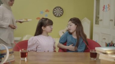 Moms bringing burgers to eat for their little girls doing schoolwork. The veiled mother and her friend bring their little daughter, who is studying together, something to eat to take a break.