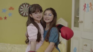 Little girl in boxing gloves and her friend are having fun together at home. Girl does boxing moves. Girl power, feminism concept. Sport, energy, activity.