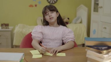 A little girl with long hair is reading a book in her room.Cute little girl reading a book, turning the page, learning, working, reading, reading a book. Portrait of little girl doing school homework.