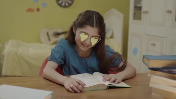 Маленькая Девочка Читает Книгу Своей Комнате Бумагами Форме Сердца Очках — стоковое видео