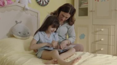 Happy cute little girl and her mother looking at childhood photos in album,recalling memories and laughing.Happy smiling mother and daughter browsing through printed family album, looking at pictures.