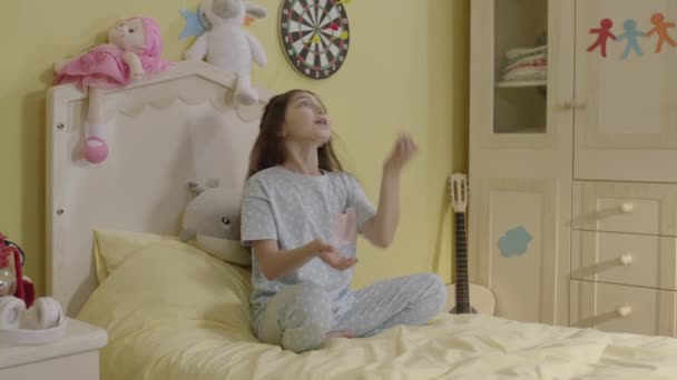 Κοριτσάκι Που Κάθεται Στο Κρεβάτι Τις Πιτζάμες Της Διασκεδάζει Πετώντας — Αρχείο Βίντεο