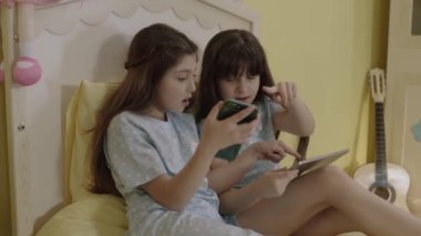 Children are surfing the internet with technological communication tools, phones and tablet computers. Girls listen to online lessons in bed, watch videos, play games.