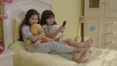 Two little sisters watching an exciting movie wrapped in their plush toys. Siblings watching tv in bed. Entertainment, Emotions, Children Watching TV, Watch Cartoons.