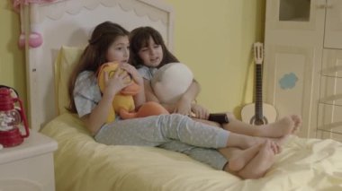 Two little sisters watching an exciting movie wrapped in their plush toys. Siblings watching tv in bed. Entertainment, Emotions, Children Watching TV, Watch Cartoons.