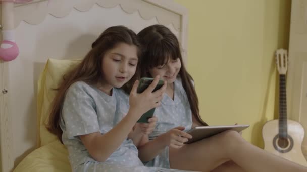 孩子们正在用技术交流工具 电话和平板电脑上网 女孩在床上听在线课程 看视频 玩游戏 — 图库视频影像
