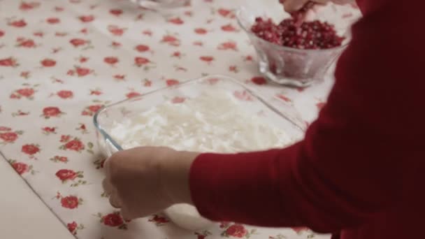 ラマダーン中にイスラム教徒によって作られた牛乳とザクロとガラスのデザート 台所のテーブルの上に甘草の上にザクロの種を投げる女性のクローズアップ手 オスマン料理のデザート — ストック動画