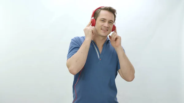 Stock image Man listening to mp3 radio music in wired headphones, listening to music and dancing in front of white background. Leisure activity. Man wearing wired headphones having fun while listening to music.