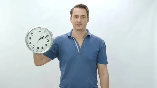 Character portrait of young man holding a large wall clock. The man shows that time passes and it is necessary to use time well. The young man draws attention to aging.