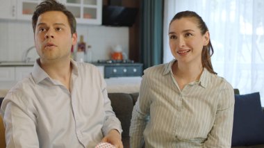 Cheerful beautiful young couple resting on sofa in modern home, talking, enjoying romantic day.Young couple laughingly looking at the empty advertising space to the left of the screen.