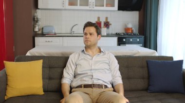 Portrait of man sitting on sofa at home. Young male enjoying lifestyle looking at camera while sitting on comfortable sofa in his apartment.