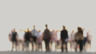 An indistinct crowd walking towards the camera in front of a white light.