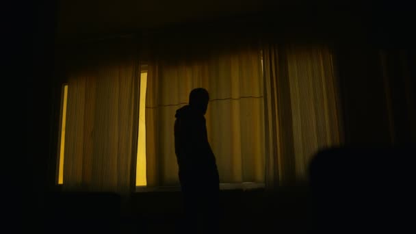 暗室に閉じられた窓の前に立っている不安そうな男が窓を開けて周りを見渡している — ストック動画