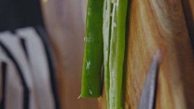 Close-up hands of woman cutting green onions on a wooden floor in the kitchen.Woman is cutting green onions in the kitchen. Slicing green onions to make sandwiches.Video for the vertical story.