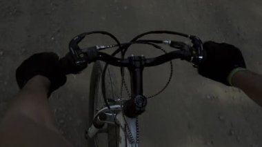 The cyclist is holding the steering wheel. A man rides a bicycle on a dirt road in the forest. Healthy lifestyle and green energy.Camera image of cyclist attached to helmet