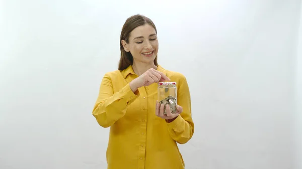 Character portrait of a young woman who likes to save money, saving money in a jar. Young healthy woman tosses coin into piggy bank, sees her savings and feels happy.