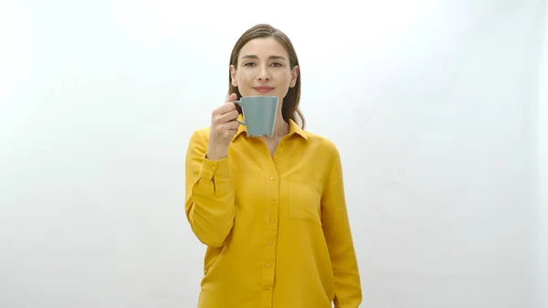 Character portrait of a young woman drinking a cup of coffee, black or green tea. Young healthy woman sniffing cup of coffee or tea isolated on white background pointing at camera