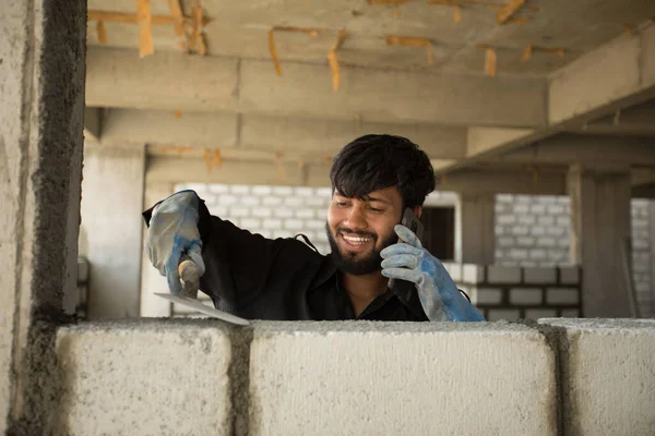Mutlu bir inşaat işçisi telefonda konuşurken beton bir duvar örer. Bir müteahhit çakı kullanarak ustalığa çimento tuğlası yerleştirir. Hızlı iş, tuğlacı.