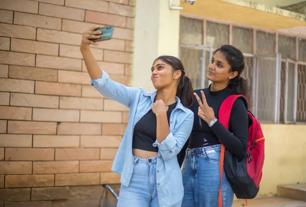 Asyalı neşeli, neşeli kızlar üniversitede boş zamanlarında selfie çekiyorlar. Üniversitede selfie çektirmek için iki kız kameraya peynir hareketi yapıyor..