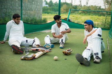 Kriket oyuncuları antrenman sırasında ağlarda otururken spor yaptıktan sonra birbirleriyle konuşuyorlar. Arkadaşlık kavramı, ara vermek ve iletişim kurmak..