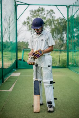 Eldiven takan kriket oyuncusu, ağlarla antrenman yapmaya hazır. Vurucu sahada topa ve atıcıya karşı koymaya hazır. Eldivenler mükemmel bir koruma ve daha iyi kavrama sağlıyor..