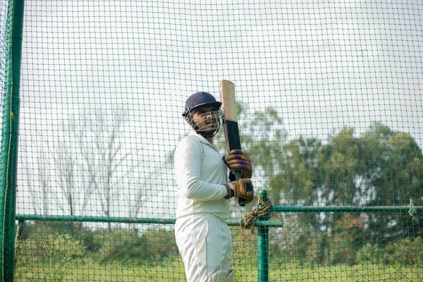 The cricket player is ready to practice batting in the nets during his practice time. Devoted cricket player prepares for intense practice session in the nets, fully committed to honing skills.