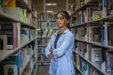 Üniversite kütüphanesinin içinde duran ve yüksek kurumlardaki kameralara bakan genç bir kız. Başarılı mükemmel öğrenici, burs, iyi kalite eğitim konsepti