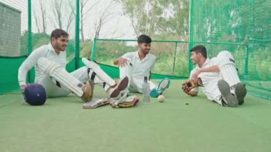Kriket oyuncusu net çalışmadan sonra takım arkadaşlarıyla sohbet ediyor. Oyuncular ağlarda ahrd eğitimi aldıktan sonra mola sırasında dinleniyorlar.