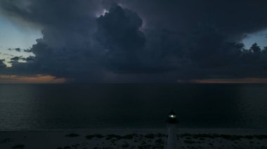 Deniz kıyısındaki uzun deniz feneri fırtınalı bir gecede ticari gemilerin seyrüsefer için yanıp sönen ışık. Okyanus üzerinde şimşekler çakan fırtına gemiler için tehlike arz ediyor..