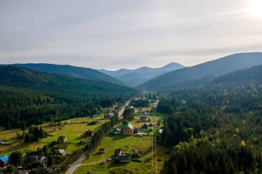 Parlak günbatımında karanlık çam ağaçları ve yüksek tepeler arasındaki küçük dağ köyleri üzerindeki sisli akşamın hava manzarası. Şafakta vahşi dağ ormanlarının inanılmaz manzarası.
