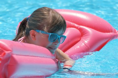 Genç neşeli kız tropikal tatillerde sıcak yaz gününde mavi suyla yüzme havuzunda şişme şişme yatakta yüzerken eğleniyor. Yaz etkinlikleri konsepti.