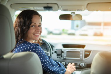 Direksiyon başında oturup araba sürerken omzunun üstünden bakan sıradan giysili çekici genç bir kadının portresi..