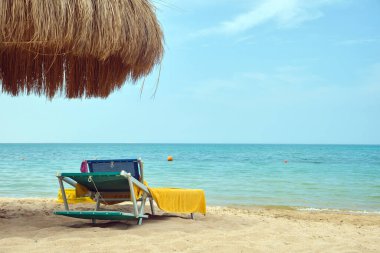 Yazın mavi renkli gökyüzüne karşı dinlenen güneşli deniz kıyılarında saman gölgesi şemsiyeleri..