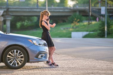 Aracının yanında duran şık kadın sürücü yazın şehir caddesinde cep telefonuyla konuşuyor..