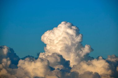 White fluffy cumulonimbus clouds forming before thunderstorm on summer blue sky. Changing stormy cloudscape weather.