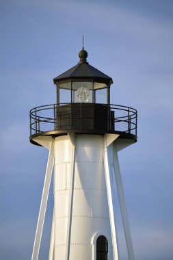 White tall lighthouse on sea shore against blue sky for commercial vessels navigation.