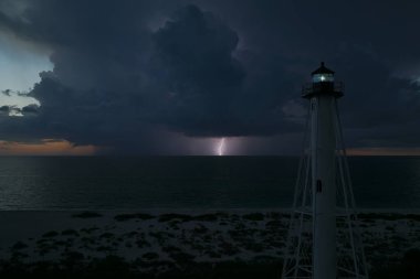 Deniz kıyısındaki uzun deniz feneri fırtınalı bir gecede ticari gemilerin seyrüsefer için yanıp sönen ışık. Okyanus üzerinde şimşekler çakan fırtına gemiler için tehlike arz ediyor..