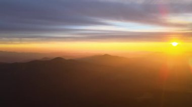 Gün batımında gün batımında parlak güneş ışınlarıyla karanlık dağ tepelerinin havadan görünüşü. Akşamları sisli tepeler ve sisli vadiler.
