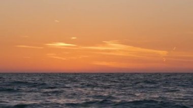 Dramatic bright red sky at ocean sunset, soft evening clouds over sea dark water.