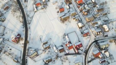 Kırsal kesimde kışın, karla kaplı çatıları olan yerleşim evleri arasında araba sürüşünün hava görüntüsü.