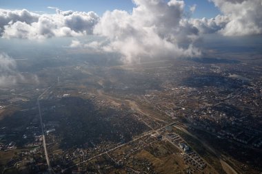 Uzak şehrin yüksek irtifasındaki uçak penceresinden hava manzarası beyaz kabarık kümülüs bulutlarıyla kaplı..
