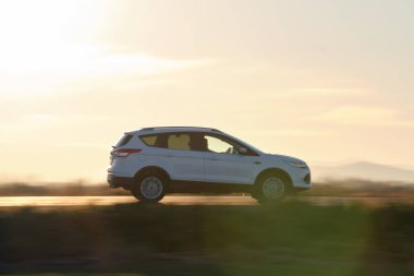 Gün batımında şehirlerarası yolda hızla giden bir SUV arabası. Akşamları otoyol trafiği.