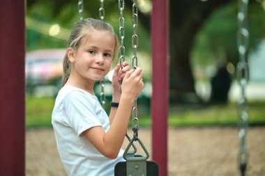 Genç, güzel, gülümseyen genç kız yaz parkında salıncaklarda tek başına oynuyor..