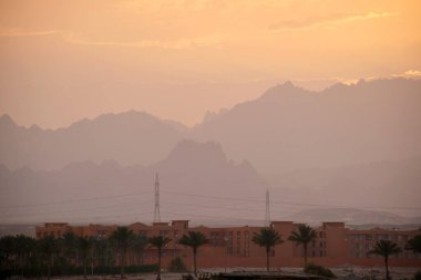 Uzak otel kompleksiyle gün batımı manzarası Mısır çölündeki karanlık dağ zirvelerine karşı.