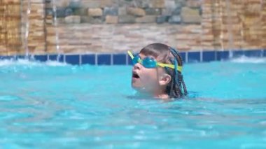 Young child girl in goggles learning to swim in blue pool water outdoors. Summer recreation activity concept.